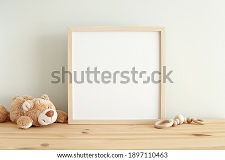 Square nursery art frame mockup, empty wooden frame on shelf in kids room interior.