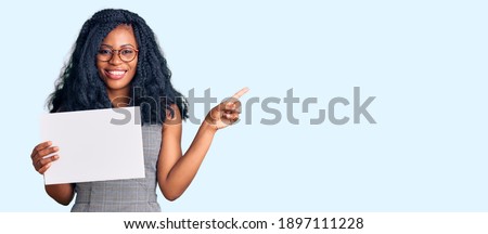 Beautiful african american woman holding blank empty banner smiling happy pointing with hand and finger to the side 