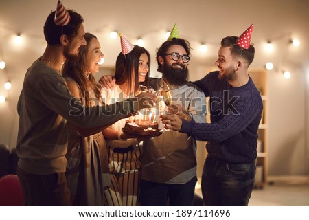 Here to you. Bunch of friends wishing Happy Birthday to young woman in her twenties, raising champagne glasses and having fun during cozy party at home or in a cafe