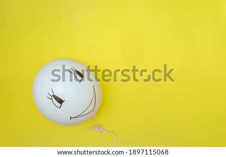 White balloon on yellow background. A funny face is drawn on the ball.