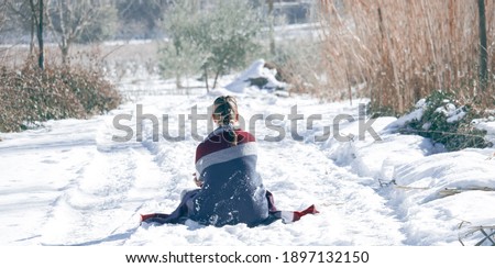 Panoramic picture of a girl's back with blonde hair that has a braid done,  is looking at the beautiful winter day while she sitting in the snow. Back view on snowy day 2021. Winter Concept. 