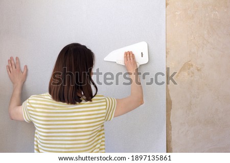 young caucasian woman with dark hair makes repairs, applies glue on the wall, glue the wallpaper, new design, home renovation, comfort, brush, apply paint, interior designer, interior design