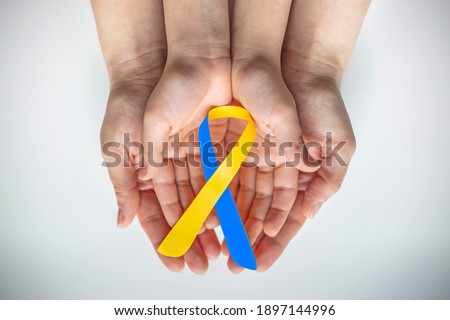 Adult and child hands holding blue and yellow ribbon shaped paper, Down syndrome awareness , World down syndrome day Royalty-Free Stock Photo #1897144996