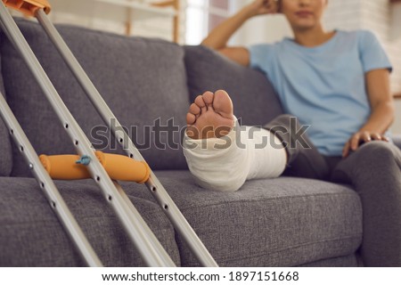 Close up of a crutches and a broken leg in a plaster cast of a woman sitting on a sofa and resting. Concept of rehabilitation after injury. Selective focus. Royalty-Free Stock Photo #1897151668