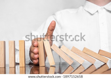 Close-up Of A Human Hand Stopping Wooden Blocks From Falling On Table. The man's hand holds the falling wooden bars. Concept: business, stability, fall, risk, collapse.