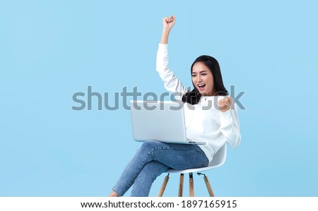 Young woman asian happy smiling celebrate. While her using laptop sitting on white chair isolate on bright blue background.