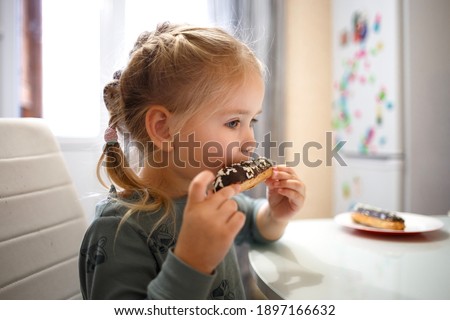 little cute girl eating cake while sitting at the kitchen table