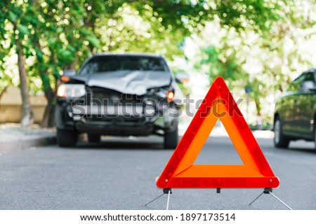Red emergency stop triangle sign on road during a car accident. Broken gray car in road traffic accident. Car crash traffic accident on city road after collision