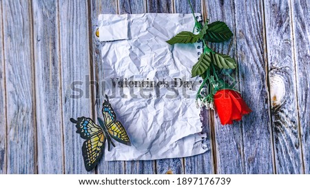 Flat lay composition with words Valentine's Day written in crumpled blank paper with rose flowers on wooden background with copy space for design, text.
