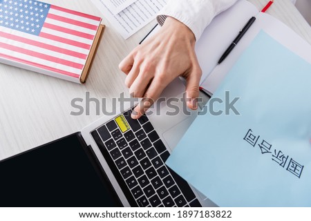 partial view of interpreter pressing translation key on laptop near paper with hieroglyphs and american english dictionary.Translation:"international contract"