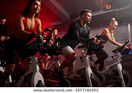 people biking in spinning class at modern gym, exercising on stationary bike. group of caucasian people athletes training on exercise bike Royalty-Free Stock Photo #1897186402