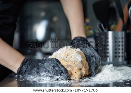 High quality photo about cook with gloved hands kneads dough on the table side view