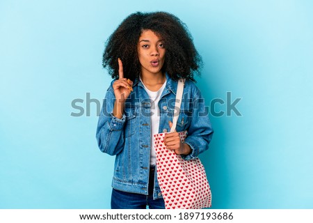 Young african american curly woman holding a valentines day fabric bag having some great idea, concept of creativity.
