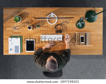 Top view of businessman working on computer at desk with paperwork in home office. Royalty-Free Stock Photo #1897198501
