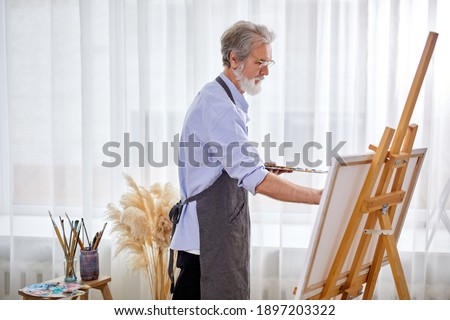 elderly artist man concentrated on painting, caucasian male in apron is immersed in the creation of art