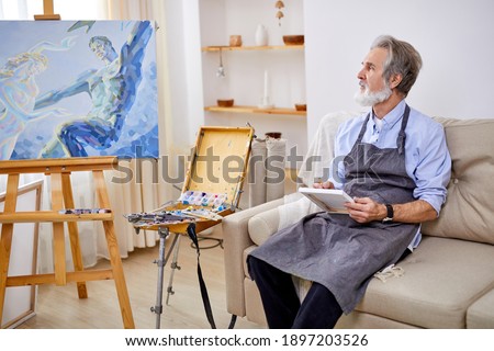 talented artist sitting on sofa and thinking, holding pencil and paper in hands, looking at side