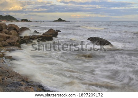 Smooth waves crashing rocks under sunset in brazilian coastline.