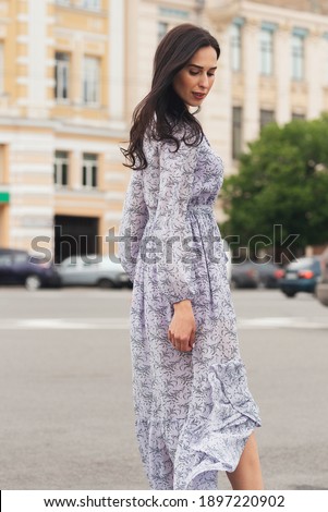 Young elegant brunett girl posing at city street. Pretty beautiful business woman in elegant dress against city background.