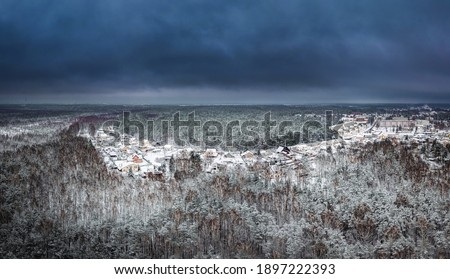 Snowy winter landscape with forest covered in snow. Aerial view over dramatic storm clouds. White scenic countryside.
