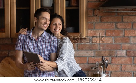 Wide banner panoramic view of smiling millennial Caucasian couple use tablet look in distance dreaming visualizing happy future together. Excited young man and woman user hold browse pad device.