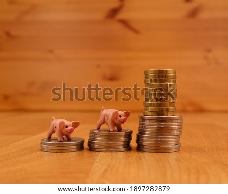 Cute miniature plastic toy pigs standing on piles of silver and golden coins. Concept of savings. Close up and isolated against a wooden background.