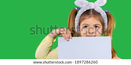 Banner. Cute little girl holding a white sheet on a green background with side space.