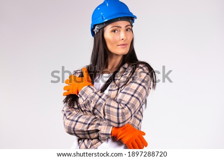  Young female mechanic in hard hat and protective builder gloves posing on a gray background. Gender equality, fearless, strong .