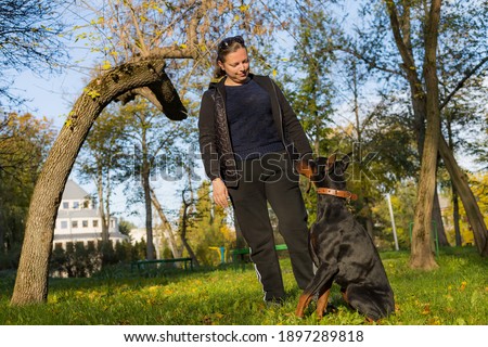 A young woman on a walk with a Doberman is enjoying talking with a pet. Selective focus with blurred background. Shallow depth of field.