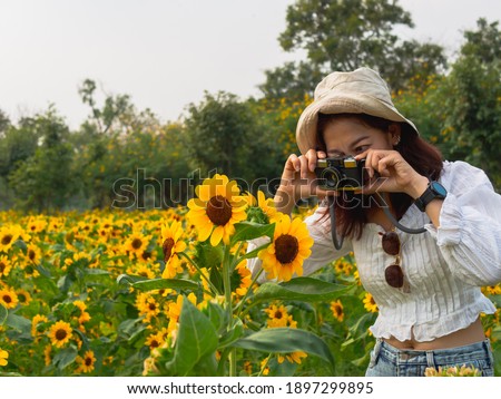 Portrait of 30-40s Asian women wearing white hats, wearing white shirts. Taking a picture with a toy camera In the park Full of green grass And sunflowers happily on a bright day With her holiday
