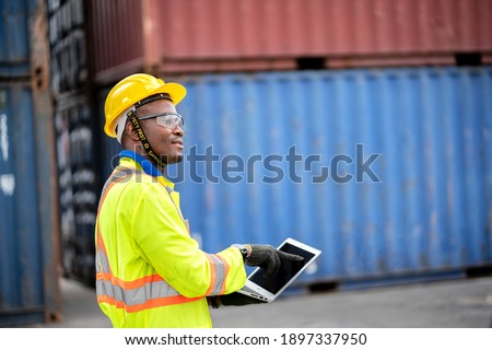 worker man in protective safety jumpsuit uniform with yellow hardhat and use laptop check container at cargo shipping warehouse. transportation import,export logistic industrial service