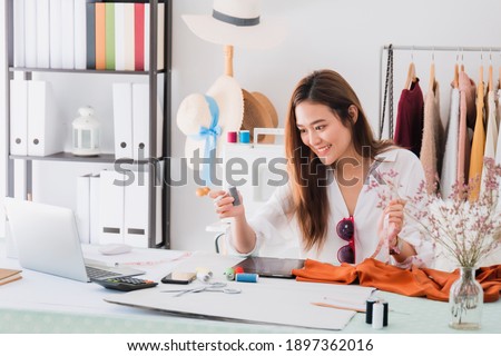 Beautiful asian woman fashion designer sitting in the clothing store and studio.In front of the laptop to meeting online.Business online influencer on social media concept.