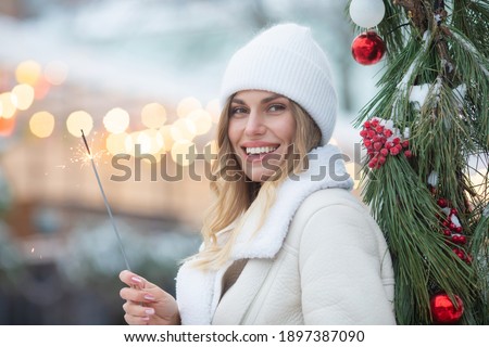 Outdoor photo of young beautiful happy smiling girl holding sparkler, walking on street. Woman wearing stylish winter clothes. Christmas, New Year, concept.