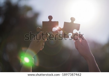 Woman hands connecting couple puzzle piece against sunrise effect, businesswoman holding wood jigsaw with sunset background. Business solutions, target, success, goals and strategy concepts