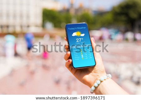 Woman outside in city checking weather forecast on her mobile phone Royalty-Free Stock Photo #1897396171