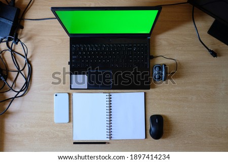 Desk with chroma green screen laptop note book pencil mobile phone mouse and cables on desk blank canvas no logos