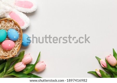 Happy easter. Multicolored eggs in a basket, tulips, a cotton branch on a gray background. Flat lay greeting card copy space.