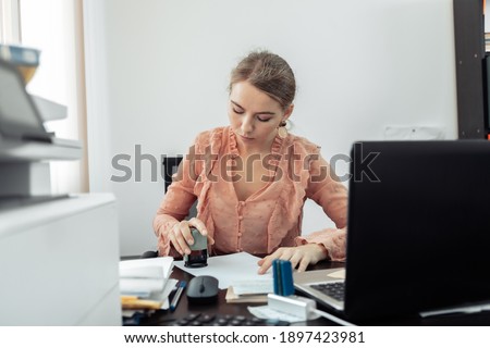 Young business woman puts a stamp on a document in her workplace