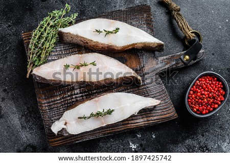 Raw fresh halibut fish steak on a wooden cutiing board. Black background. Top view.