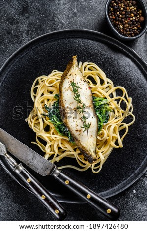 Spaghetti pasta with Halibut fish steak and spinach. Black background. Top view.