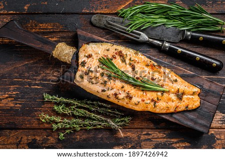 Baked trout fillet on a cutting board. Dark wooden background. Top view. Royalty-Free Stock Photo #1897426942