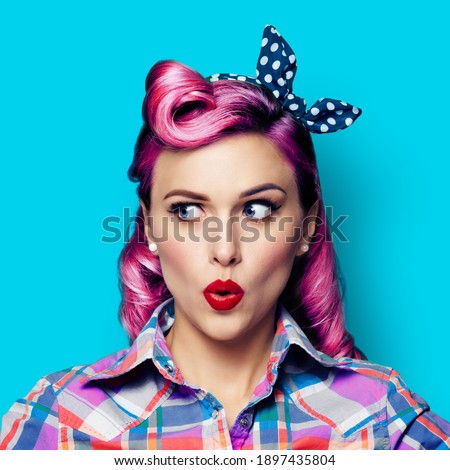 Excited surprised woman. Pinup girl looking sideways. Purple head model at retro fashion and vintage concept. Aqua blue color background. Square composition image. 