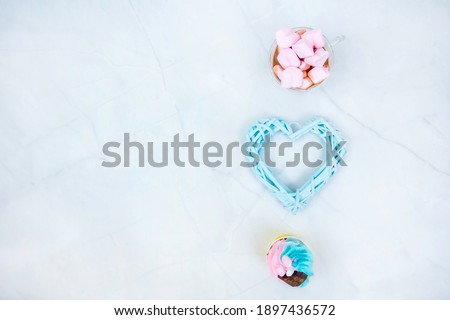 cupcake in pink and blue tones heart number 14 for Valentine's day and cocoa with pink marshmallow in a transparent mug on a light marble background