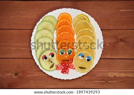 orange with eyes beautifully decorated slices of fresh fruit on a round white plate. orange, lemon, pear. on a wooden background. holiday concept. place for text