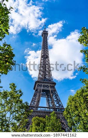 The Eiffel Tower surrounded by tree leaves in Paris, France with white clouds in the background