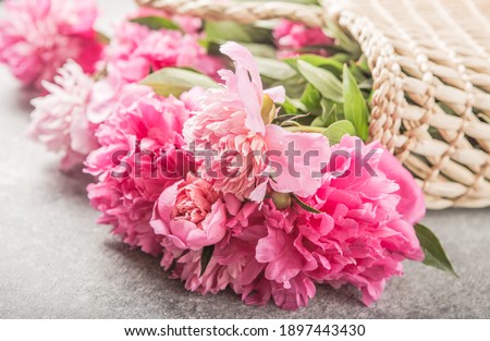 Straw bag with pink peony flowers on grey background. Flat lay, top view summer floral   concept. Hello summer. International womens day. Happy mothers day. Greeting card mockup.