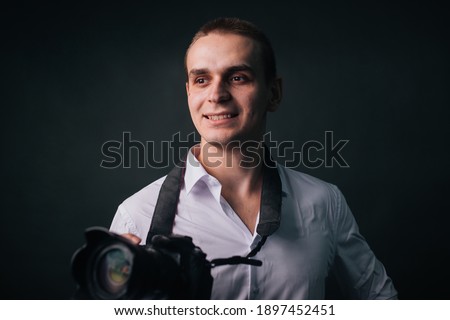 Photographer on a gray background. A man in a white shirt holds a camera in his hands.