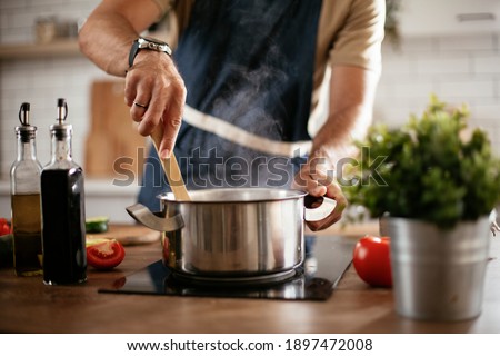 Young man cooking lunch at home. Handsome man preparing delicious food.  Royalty-Free Stock Photo #1897472008