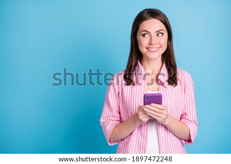 Photo portrait of happy woman looking at blank space holding phone in two hands isolated on pastel blue colored background