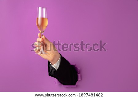 Male hand holding champagne flute breaks through purple background