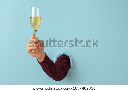 Male hand with champagne flute breaks through blue background